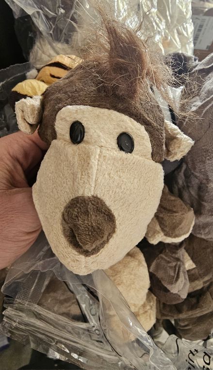 A soft toy monkey with a tuft of hair held up in front of the bag of other toys.